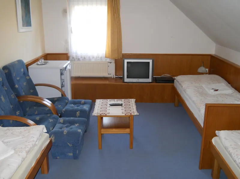 Pokoj s modrými křesly, stolkem, televizí a postelemi pod šikmým stropem